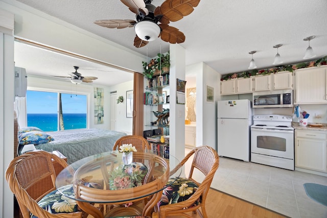 dining room with a water view, light wood-style floors, ceiling fan, and a textured ceiling