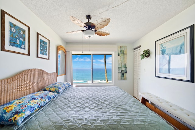 bedroom featuring a water view, a textured ceiling, a closet, and a ceiling fan