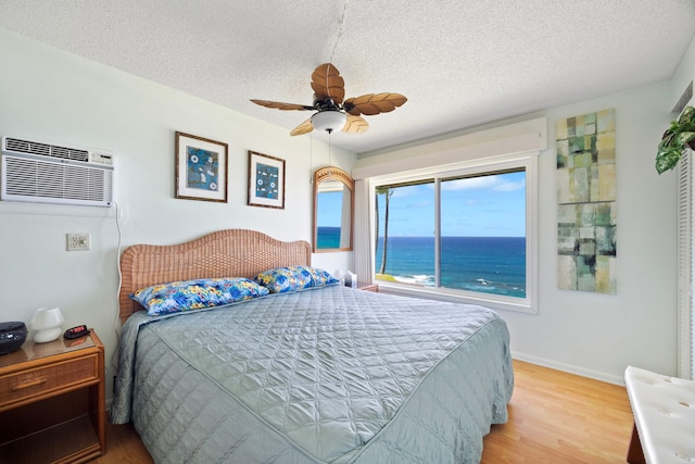 bedroom with light wood finished floors, a textured ceiling, baseboards, and a wall mounted AC