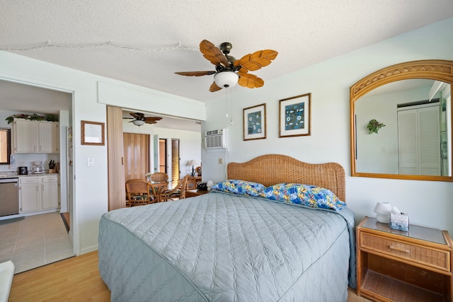 bedroom featuring a ceiling fan, a wall mounted air conditioner, light wood-style flooring, and a textured ceiling