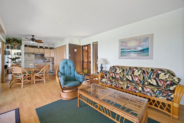 living area featuring light wood finished floors, ceiling fan, and a textured ceiling