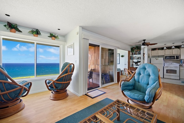 interior space with a textured ceiling, light wood finished floors, ceiling fan, a water view, and baseboards