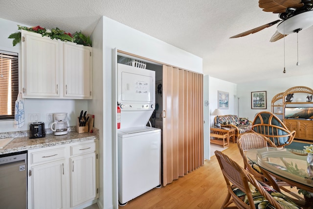 laundry area featuring stacked washer and clothes dryer, light wood-style flooring, a ceiling fan, laundry area, and a textured ceiling