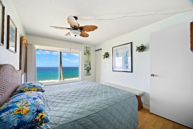 bedroom with a closet, a textured ceiling, ceiling fan, a water view, and light wood-style floors