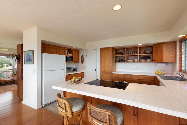 kitchen with freestanding refrigerator, a sink, open shelves, brown cabinetry, and black electric stovetop