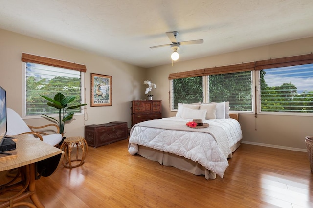 bedroom with multiple windows, light wood-style floors, baseboards, and ceiling fan
