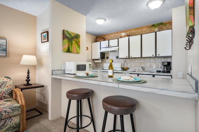 kitchen with white appliances, under cabinet range hood, a peninsula, white cabinets, and a breakfast bar area