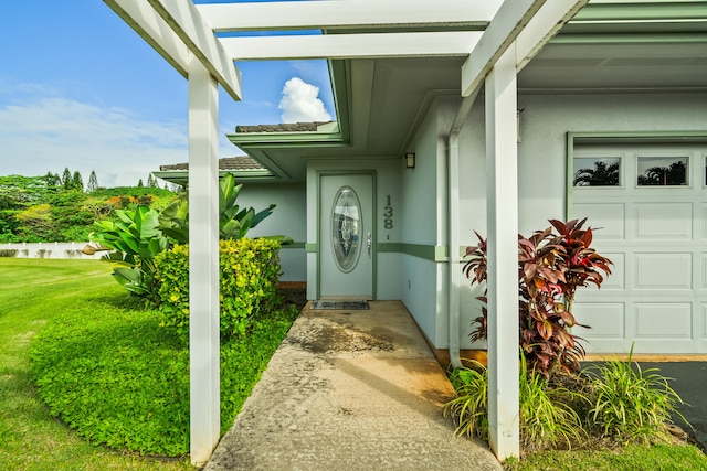 property entrance featuring stucco siding, an attached garage, and a yard