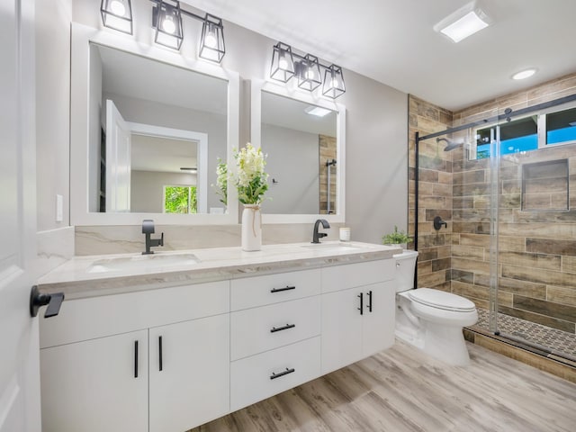 bathroom featuring toilet, a shower stall, double vanity, and wood finished floors