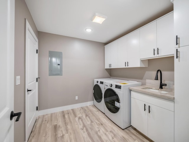 clothes washing area with electric panel, washing machine and dryer, cabinet space, light wood-style flooring, and baseboards