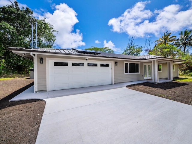 single story home featuring french doors, driveway, an attached garage, metal roof, and solar panels