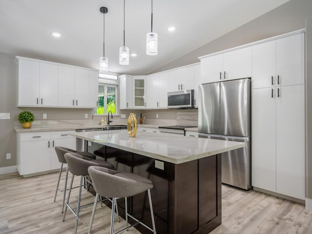 kitchen featuring stainless steel appliances, lofted ceiling, light wood-style flooring, a breakfast bar area, and decorative light fixtures