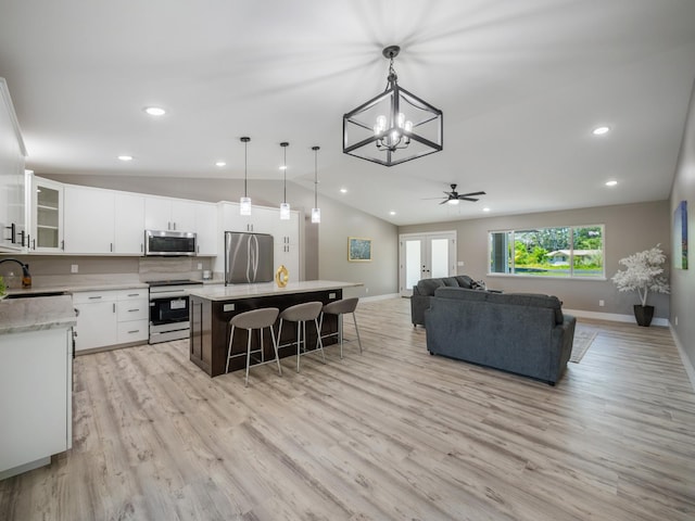 living room featuring lofted ceiling, a chandelier, light wood-style flooring, baseboards, and ceiling fan