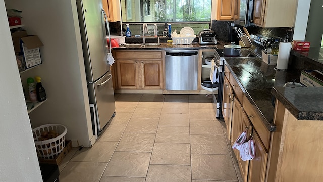kitchen with appliances with stainless steel finishes, a sink, decorative backsplash, brown cabinetry, and dark stone countertops