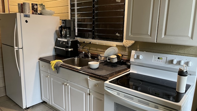 kitchen with white appliances, light tile patterned floors, backsplash, dark countertops, and a sink