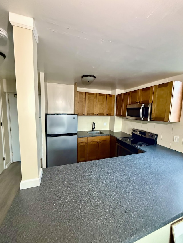 kitchen with brown cabinetry, dark countertops, appliances with stainless steel finishes, and a sink