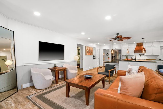 living room featuring light wood-style floors, a ceiling fan, recessed lighting, and a decorative wall