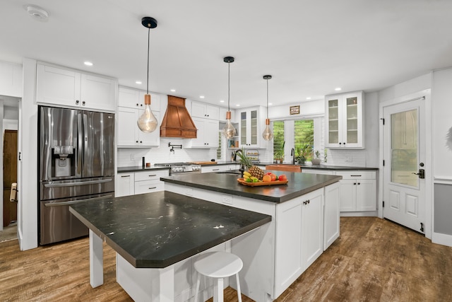 kitchen with stainless steel appliances, dark countertops, premium range hood, a sink, and a kitchen island with sink