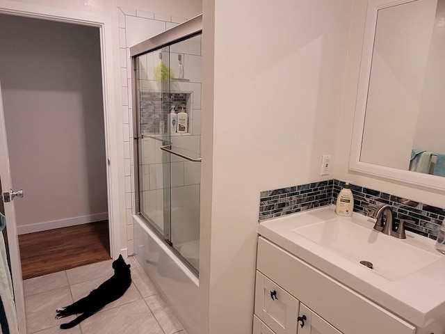 full bath with tile patterned flooring, vanity, bath / shower combo with glass door, baseboards, and tasteful backsplash