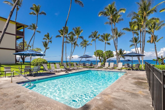 community pool featuring fence, a patio area, and a water view