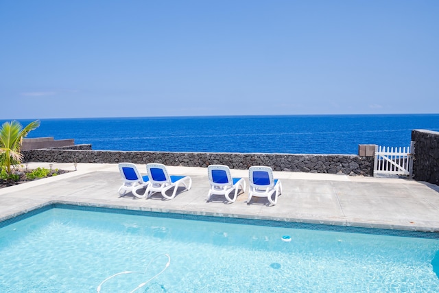 view of pool featuring a water view, fence, and a patio
