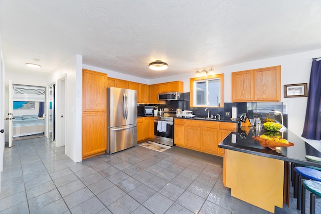 kitchen featuring stainless steel appliances, a sink, backsplash, dark countertops, and dark tile patterned floors