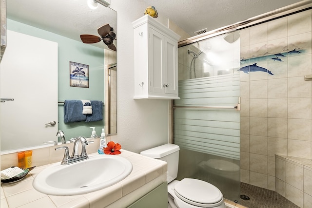 full bath with a shower stall, toilet, ceiling fan, a textured ceiling, and vanity