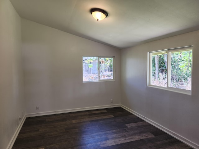 spare room featuring lofted ceiling, dark wood-style floors, and baseboards