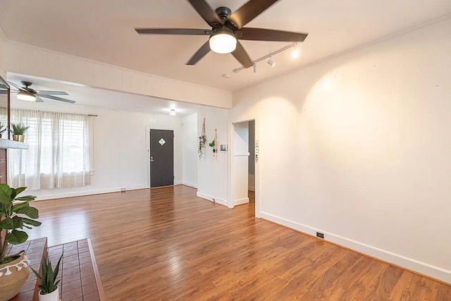 unfurnished living room with ceiling fan, track lighting, wood finished floors, and baseboards