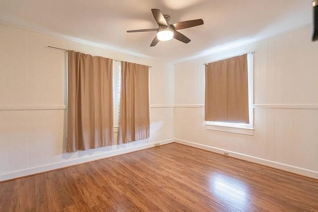 empty room with ceiling fan, wood finished floors, ornamental molding, and baseboards