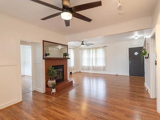 unfurnished living room featuring a ceiling fan, wood finished floors, a brick fireplace, baseboards, and ornamental molding