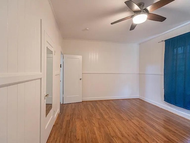 empty room featuring crown molding, wood finished floors, ceiling fan, and a decorative wall