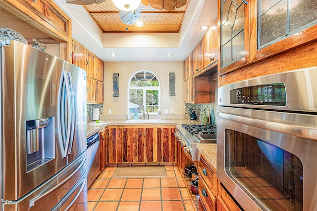 kitchen featuring stainless steel appliances, a tray ceiling, a sink, backsplash, and recessed lighting