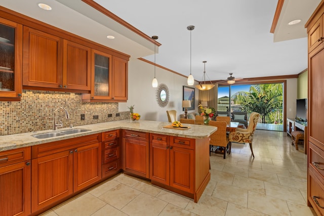 kitchen with a sink, backsplash, a peninsula, a ceiling fan, and light stone counters