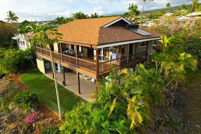back of house featuring roof with shingles, a patio, solar panels, and a deck