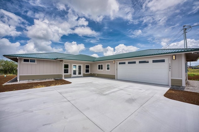ranch-style home featuring french doors, driveway, an attached garage, metal roof, and board and batten siding