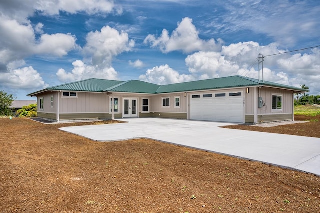 single story home featuring french doors, metal roof, an attached garage, board and batten siding, and concrete driveway
