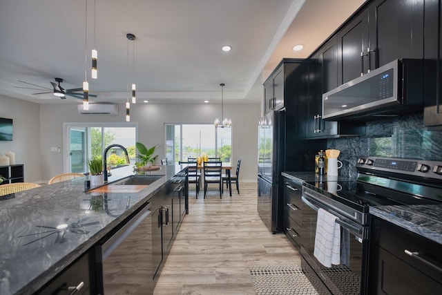 kitchen with appliances with stainless steel finishes, a sink, dark cabinets, dark stone countertops, and recessed lighting