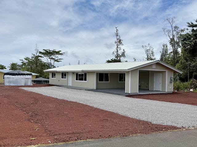 ranch-style home with gravel driveway, metal roof, an attached carport, and covered porch