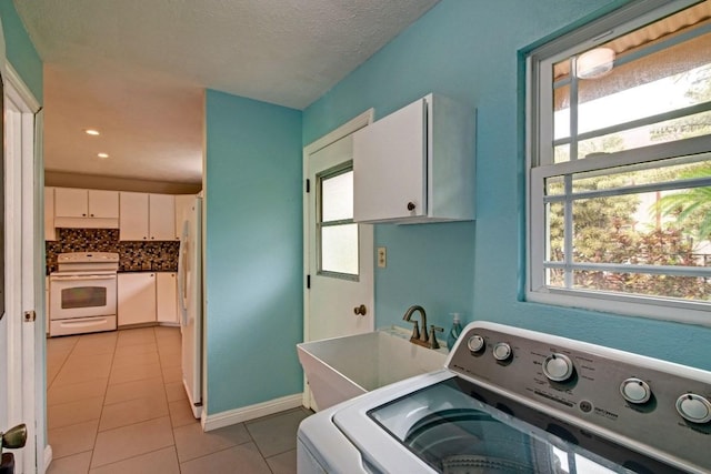 clothes washing area featuring light tile floors, a textured ceiling, cabinets, washer / dryer, and sink