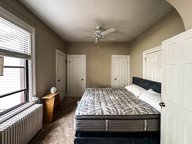 bedroom with dark carpet, radiator, multiple closets, and ceiling fan