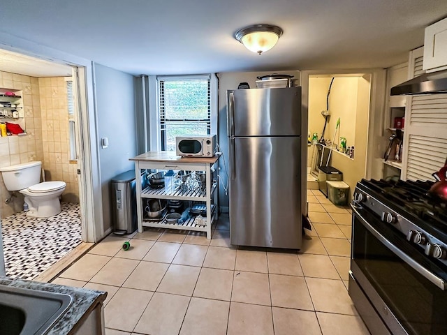 kitchen with white cabinetry, light tile patterned flooring, tile walls, and appliances with stainless steel finishes