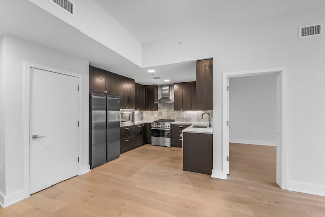 kitchen featuring dark brown cabinetry, sink, wall chimney exhaust hood, backsplash, and appliances with stainless steel finishes