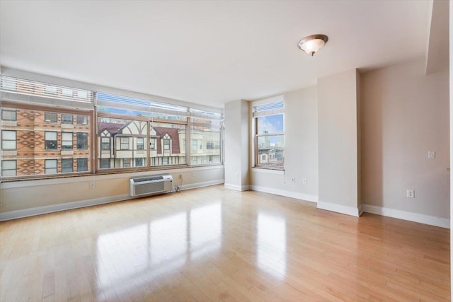 unfurnished room with baseboards, a wall unit AC, and wood finished floors