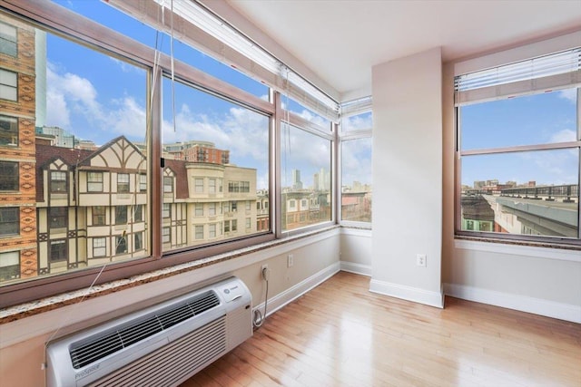 unfurnished sunroom with a wealth of natural light, a city view, and a wall mounted air conditioner