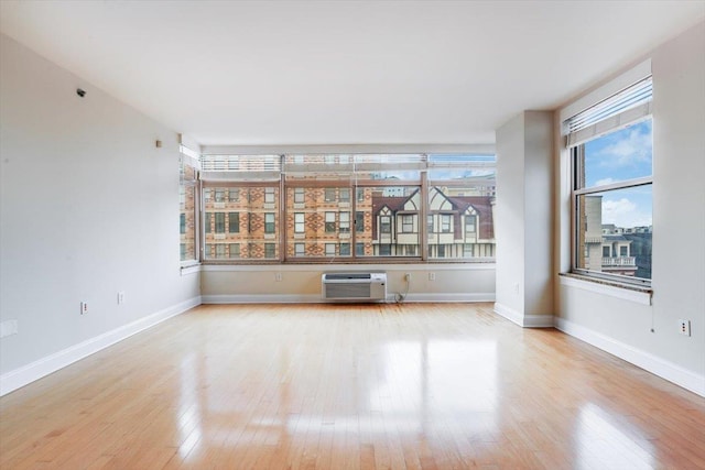 unfurnished room with light wood finished floors, an AC wall unit, and baseboards