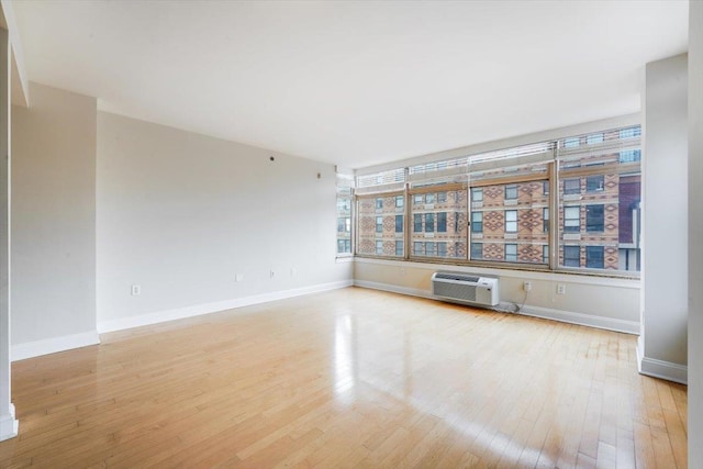 spare room featuring light wood-style flooring, baseboards, and a wall unit AC