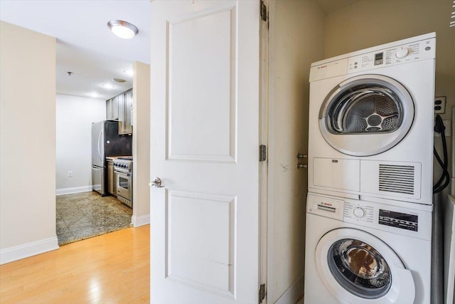 laundry room featuring laundry area, stacked washer and clothes dryer, baseboards, and light wood-style floors