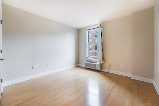 spare room with cooling unit, baseboards, and light wood finished floors