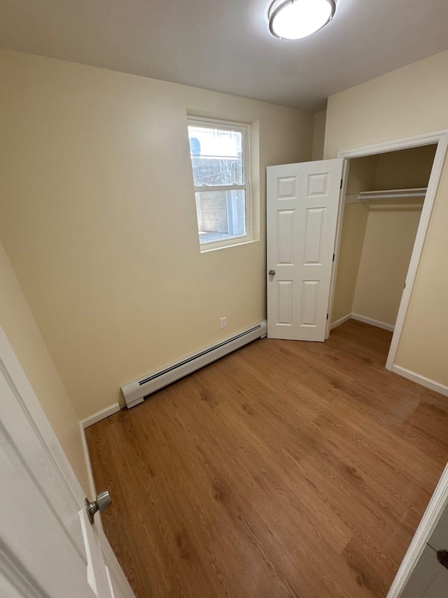 unfurnished bedroom with a closet, light wood-type flooring, a baseboard radiator, and baseboards